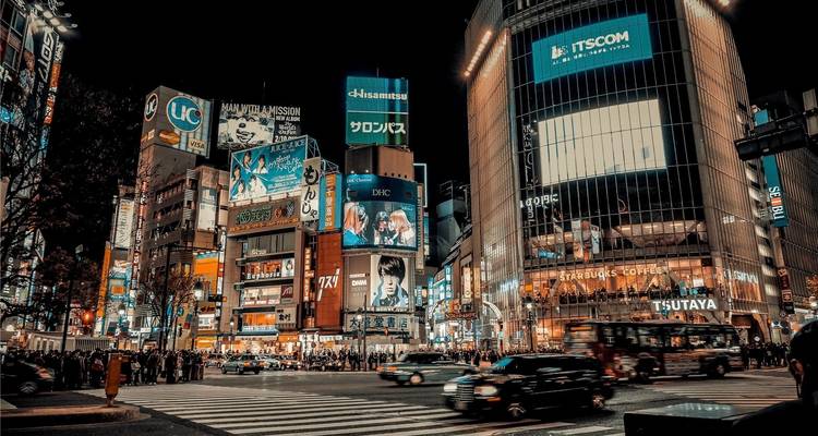 Nachtansicht der neonbeleuchteten Shibuya Crossing, die mit Menschen und Verkehr gefüllt ist, in Tokio