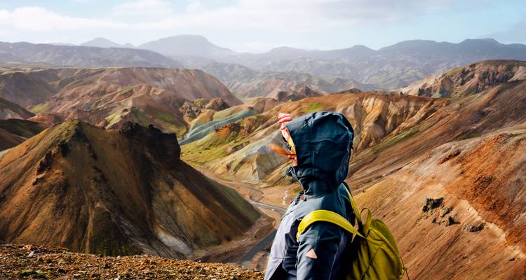Excursionista con chaqueta con capucha y mochila amarilla contempla las coloridas colinas y valles de riolita de Landmannalaugar.