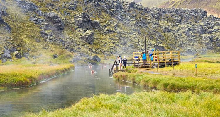 Ruisseau géothermique entouré de roches de lave mousseuses où les randonneurs se baignent dans l'eau chaude dans les hautes terres islandaises.