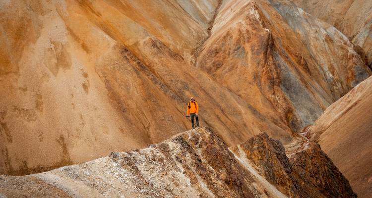 Un trekker solitaire en orange se tient sur la crête acérée des parois spectaculaires d'un canyon de rhyolite aux lumières tamisées.
