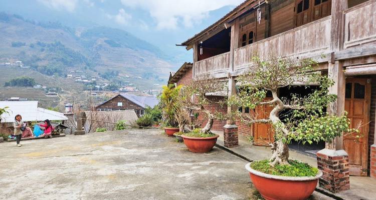 Traditional wooden house with potted trees and hills in the background.