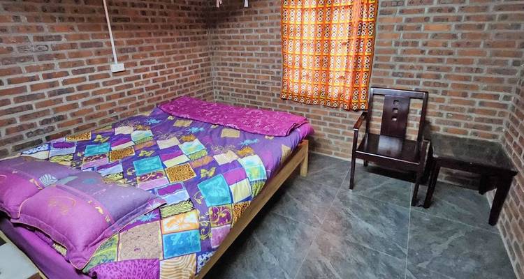 Bedroom with brick walls, colorful bedding, and a wooden chair.
