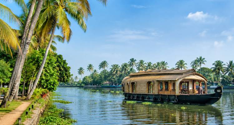 Traditional wooden houseboat cruising the lush palm-lined backwaters under a sunny sky.