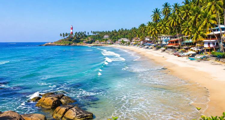 Sweeping tropical beach with lighthouse, palm trees and colourful seaside village along turquoise water.