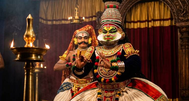 Vibrant Kathakali dancers performing in ornate costumes and dramatic makeup before brass oil lamps.