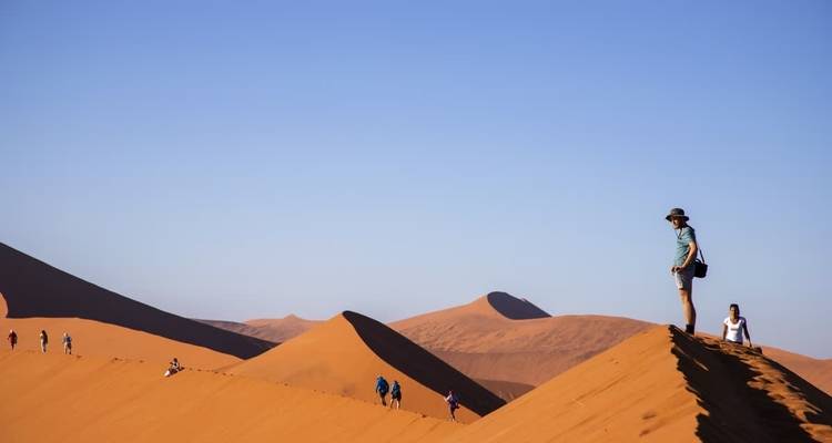 Touristen wandern auf Sanddünen bei klarem Himmel.