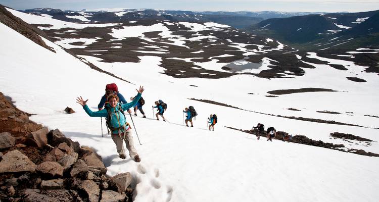Eine Reihe von Trekkern erklimmt einen verschneiten Hang in leuchtender Ausrüstung vor einer imposanten Alpinen Kulisse.