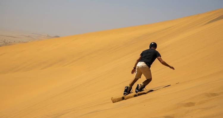 Persona haciendo sandboard en una duna de arena grande.