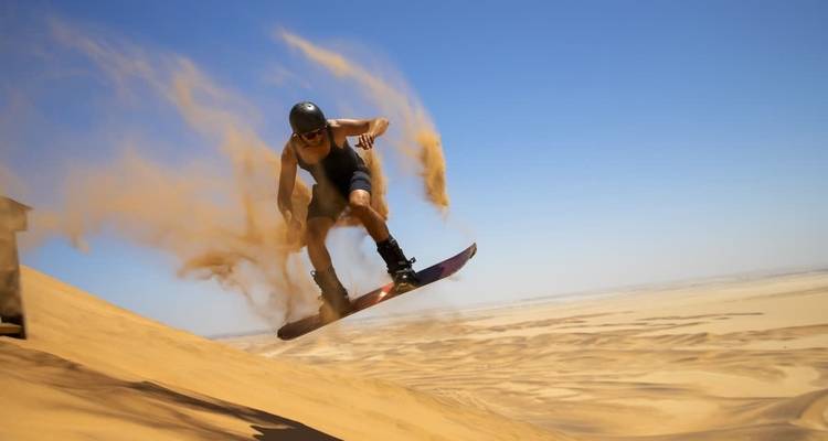 Persona haciendo sandboard con arena volando alrededor.