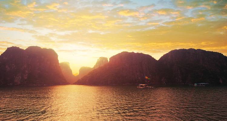 Puesta de sol dorada sobre el agua con espectaculares formaciones rocosas.