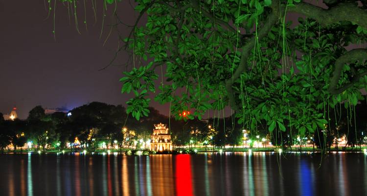 Una vista nocturna de un parque muy iluminado al otro lado de un lago.