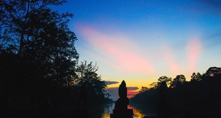 Bunter Sonnenuntergang über dem Wasser mit silhouettierten Bäumen und Strukturen.