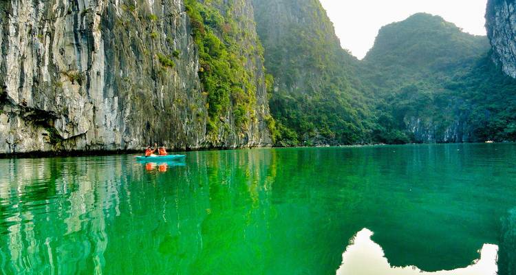 Two people kayaking on turquoise waters surrounded by steep cliffs.