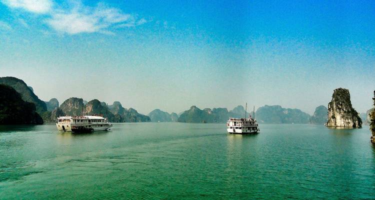Cruise boats on a wide expanse of calm water with limestone karsts in the distance.