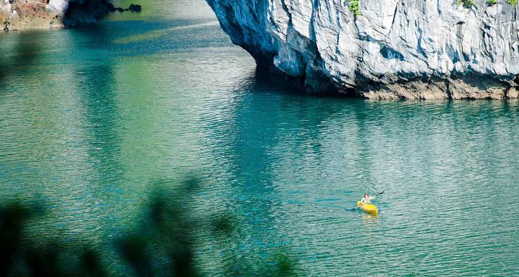 Una persona navega en kayak por aguas verde esmeralda cerca de un acantilado rocoso.