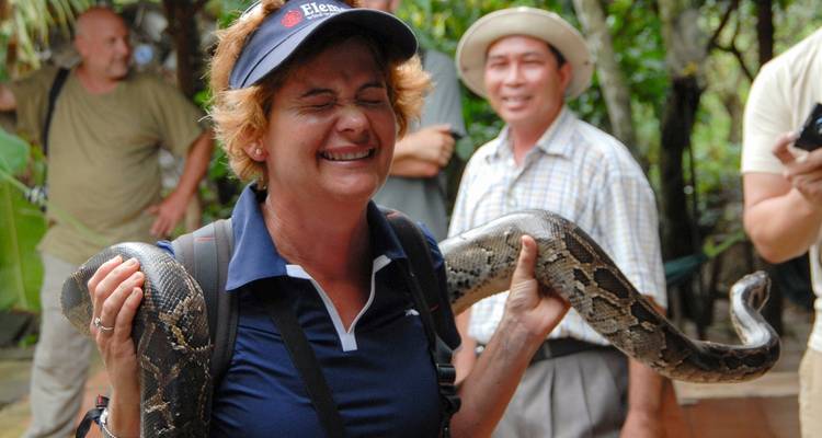Vrouw die een slang vasthoudt in een levendige jungle-omgeving, nerveus glimlachend.