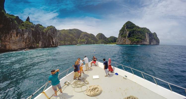 Personas en la cubierta de un barco mirando el paisaje de una isla tropical.