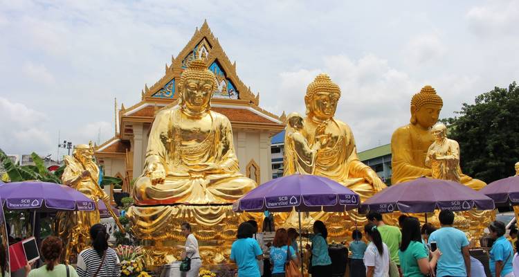 Personas caminando junto a una fila de grandes estatuas doradas de Buda afuera de un templo.