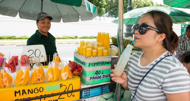 Une femme buvant du jus à un étal de rue avec des fruits frais.