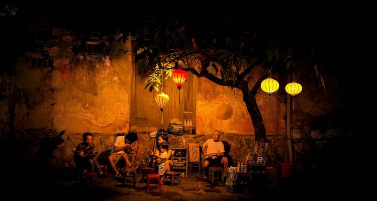 Personas cenando y relajándose bajo faroles por la noche.