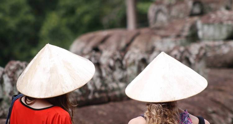 Dos personas usando sombreros asiáticos tradicionales frente a una formación rocosa.