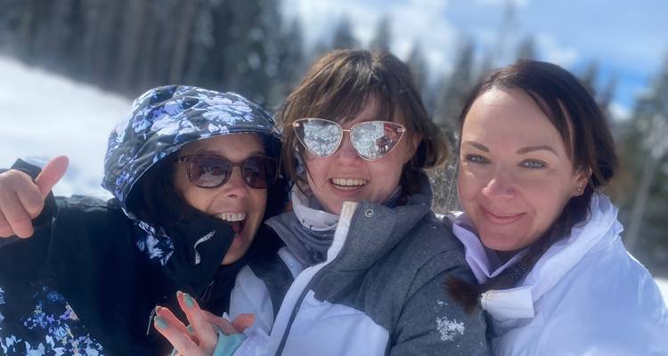 Three women posing in the snow with sunglasses.