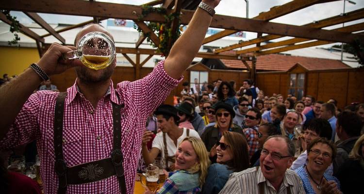 Multitud disfrutando de una animada fiesta, con un hombre brindando de pie sobre una mesa.