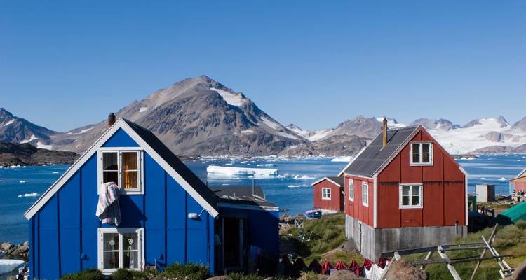 Des maisons colorées au bord de l'eau avec des montagnes en arrière-plan.