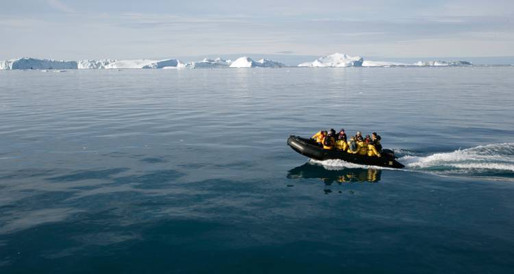 Des personnes dans un bateau sur l'océan avec des icebergs en arrière-plan.