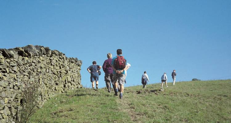 Groupe de randonneurs marchant en montée le long d'un mur de pierre