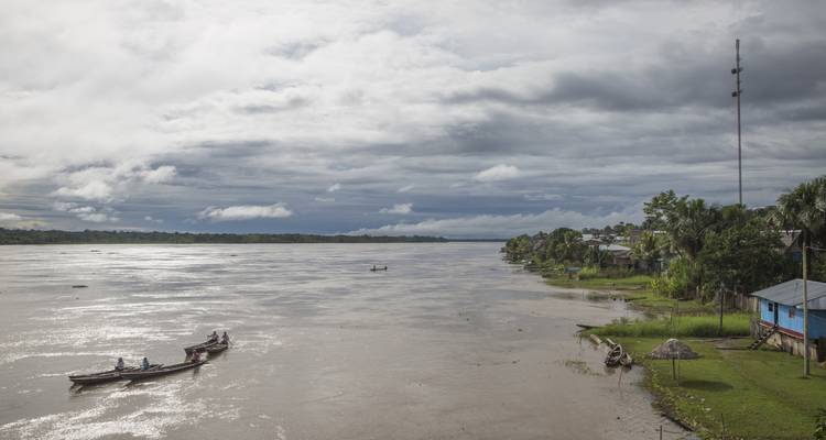 Bateaux sur une large rivière avec un village le long de la rive.
