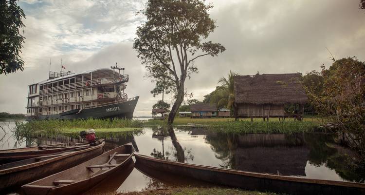 Bateau fluvial amarré à côté d'un village de jungle avec des pirogues creusées et des cabanes au toit de chaume au lever du jour