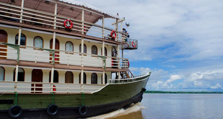 Vue latérale d'un bateau de croisière multi-ponts sur l'Amazone fendant les eaux brunes du fleuve sous un ciel bleu
