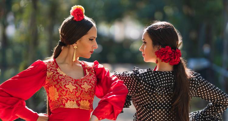 Zwei Flamencotänzerinnen in traditionellen roten und schwarzen Kleidern stehen sich in eleganter Haltung gegenüber.