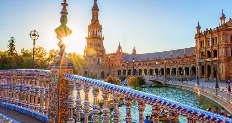 Sonnenstrahlen über der Plaza de España, die die ornamentale Kachelung der Brücke und das prächtige Palastgebäude hervorheben.