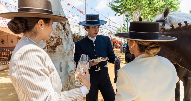 Elegant gekleidete Einheimische genießen Tapas und Sherry neben einem Pferd auf einem festlichen andalusischen Jahrmarkt.