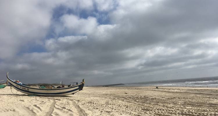 Bateau en bois sur une plage de sable sous un ciel nuageux.