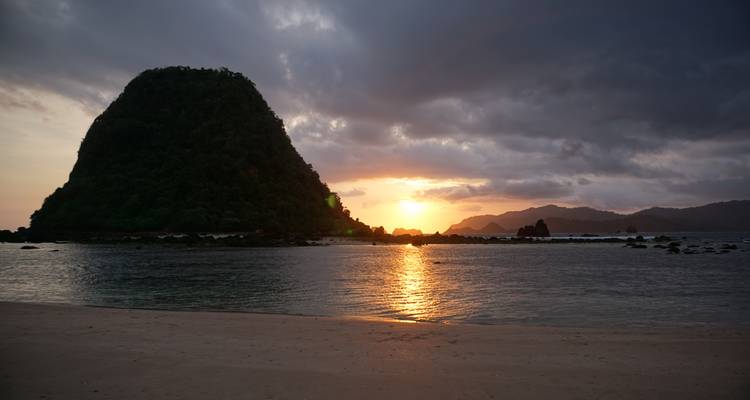 Dramatische zonsondergang boven een afgelegen tropische baai met een beboste zeestack die zich tegen de hemel aftekent