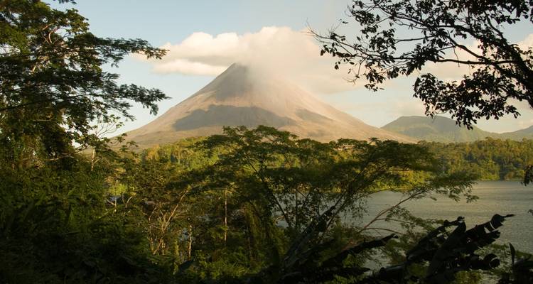 Ikonischer Vulkan Arenal, der sich über einem See erhebt, der von üppiger Regenwaldvegetation umrahmt wird.