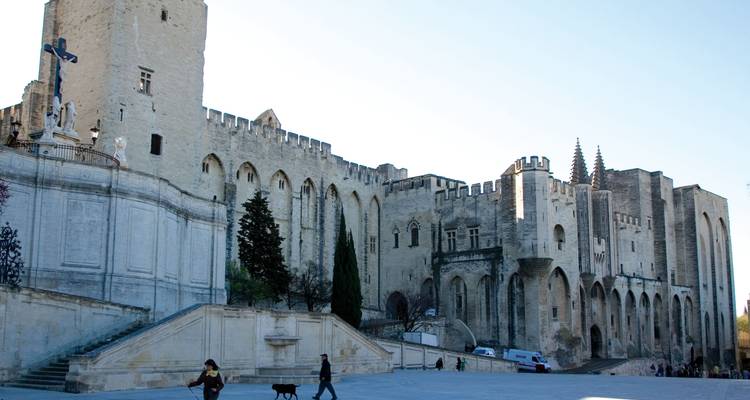 Bâtiment historique avec une grande façade en pierre et une architecture gothique, personnes marchant au premier plan.