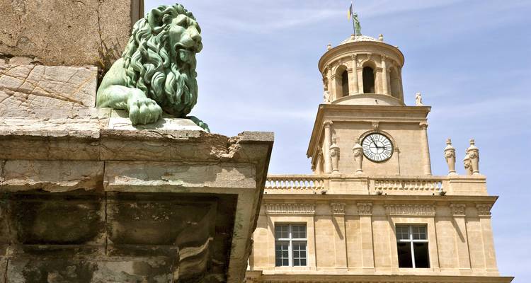 Statue de lion devant une tour d'horloge à l'architecture néoclassique.