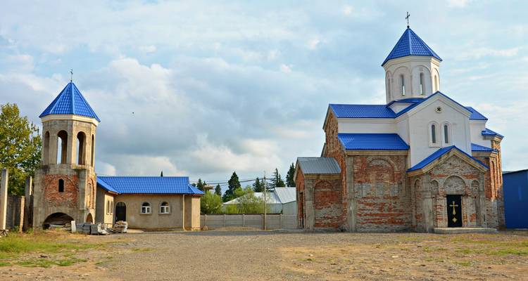 Church and bell tower with blue roofs set against a cloudy sky.