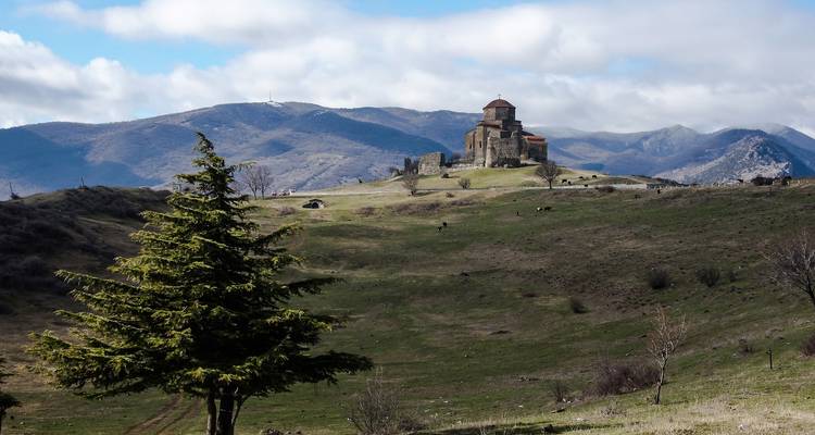 Distant view of a monastery on a hill with mountainous backdrop.