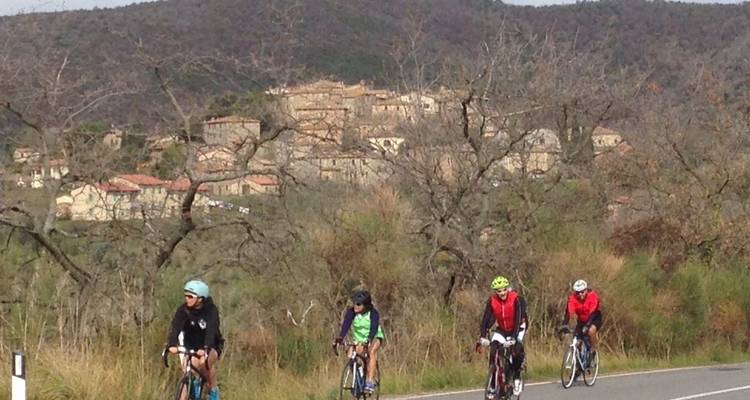 Grupo de ciclistas en una carretera rural con un pueblo al fondo.
