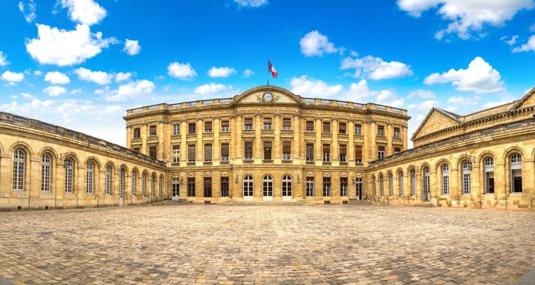 Grand bâtiment historique avec une cour et un drapeau français.