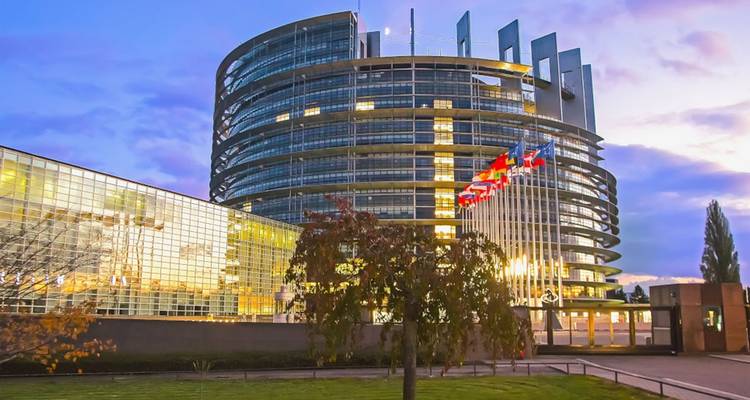 Edificio moderno del Parlamento Europeo con múltiples banderas.