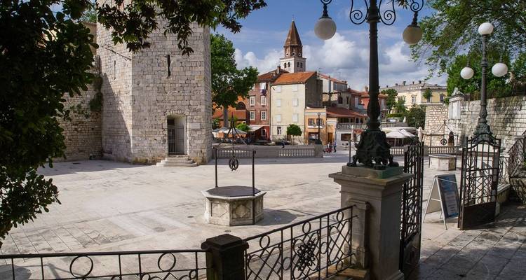 Plaza histórica con un pozo de piedra y edificios circundantes.