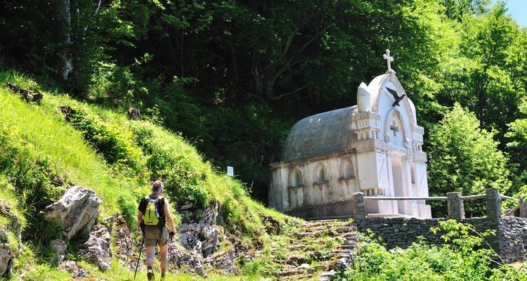 Randonneur s'approchant d'une petite chapelle dans une zone boisée.