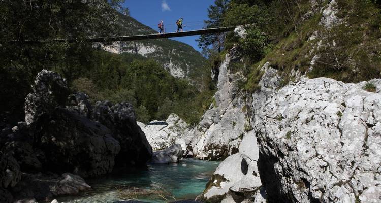 Deux personnes traversent un pont suspendu au-dessus d'une rivière turquoise.