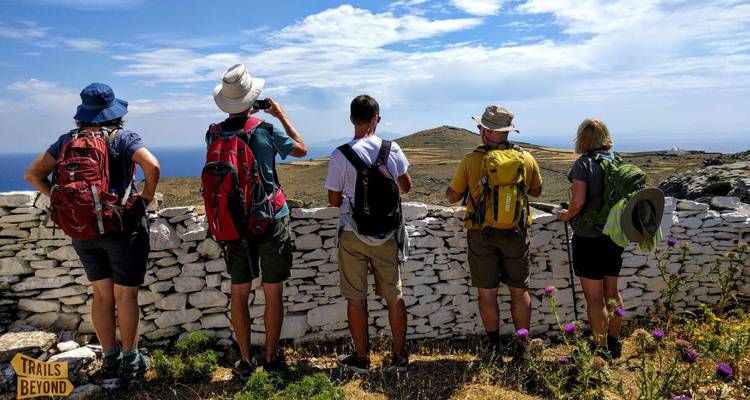 Grupo de excursionistas junto a un muro de piedra con vistas a un paisaje.